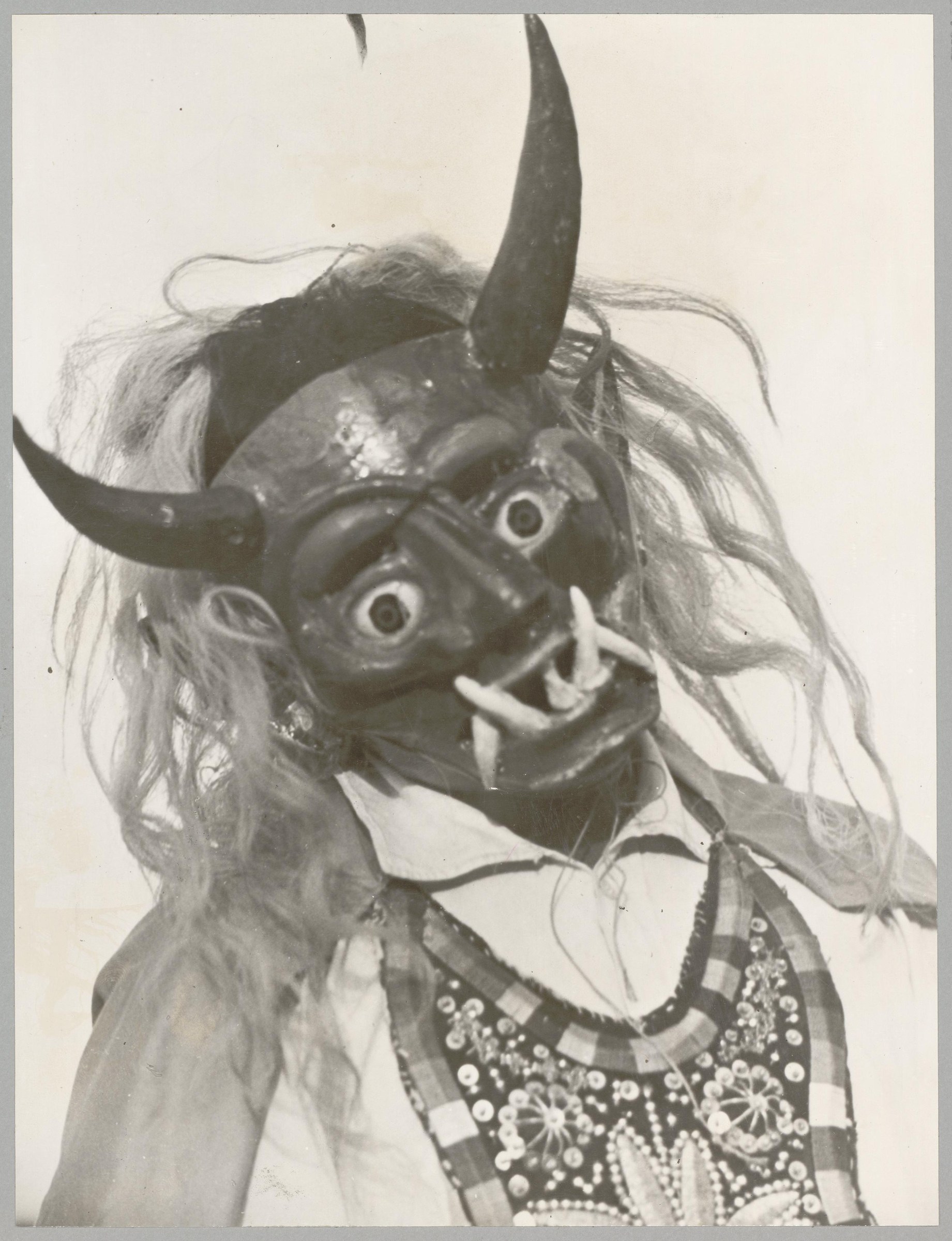 Carved wooden devil mask with long horns and hair, wearing ornate patterned costume visible below the face.