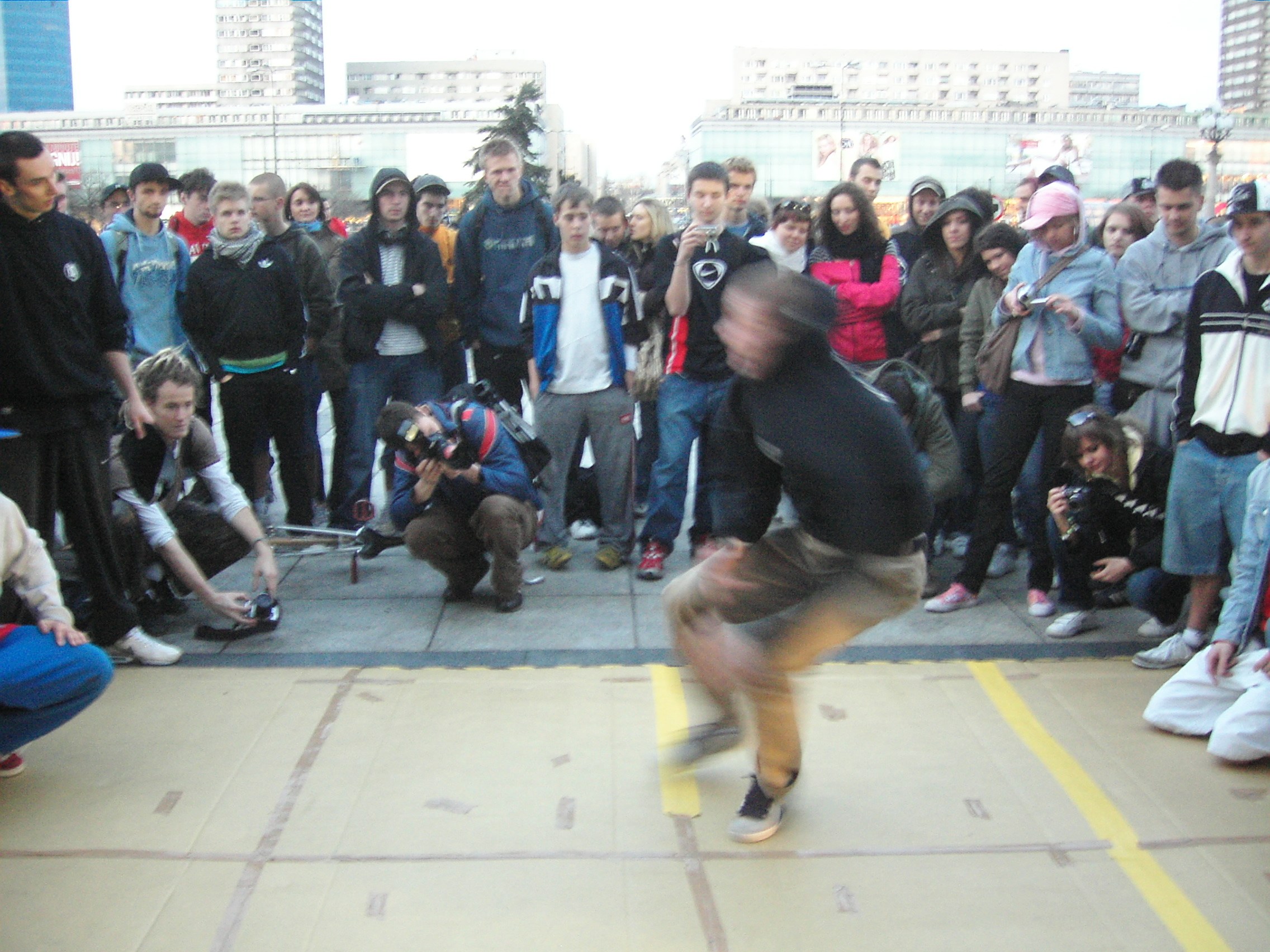 Breakdancer in inverted position performing in a circle of spectators in an urban Warsaw plaza, 2007.