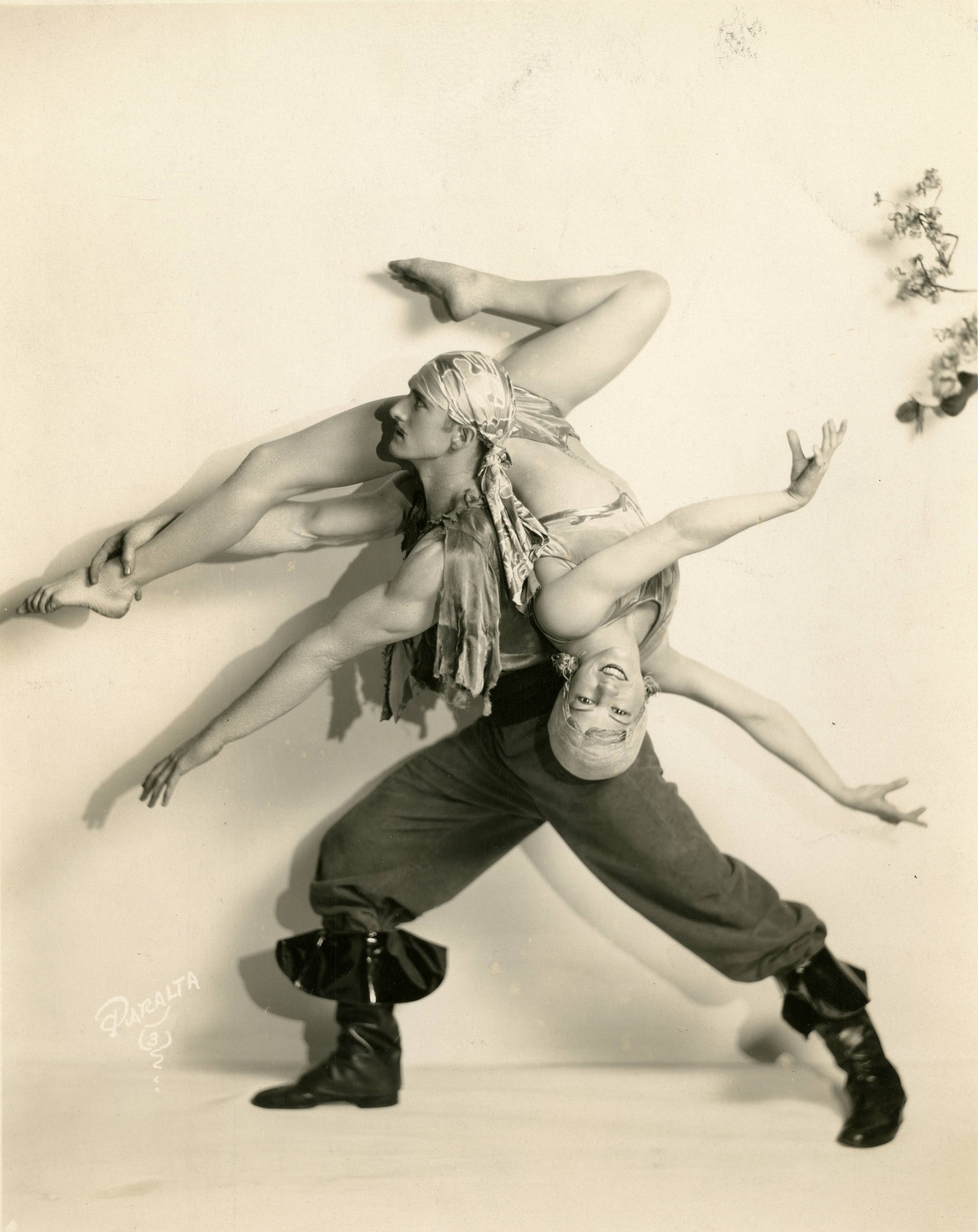 Two acrobatic dancers interlocked in an inverted position, photographed from above against a white studio backdrop.
