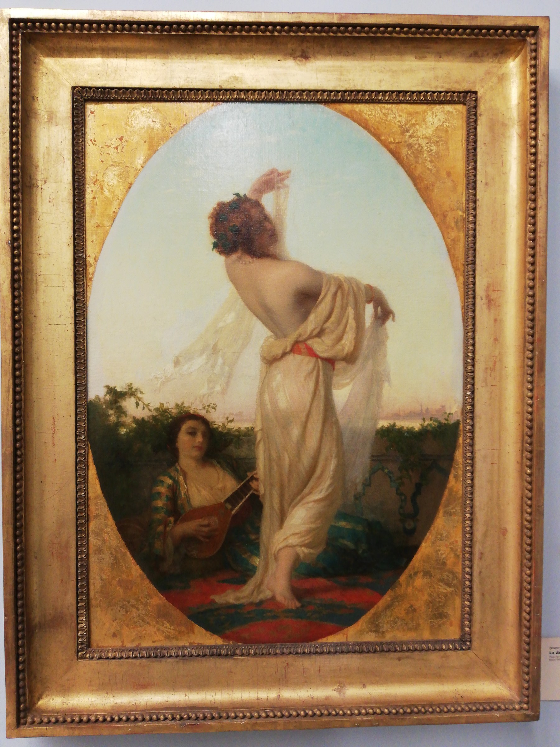 Oil painting of a standing woman in pale drapery with raised arm, twisting contrapposto pose, attended by a seated musician holding a stringed instrument in an