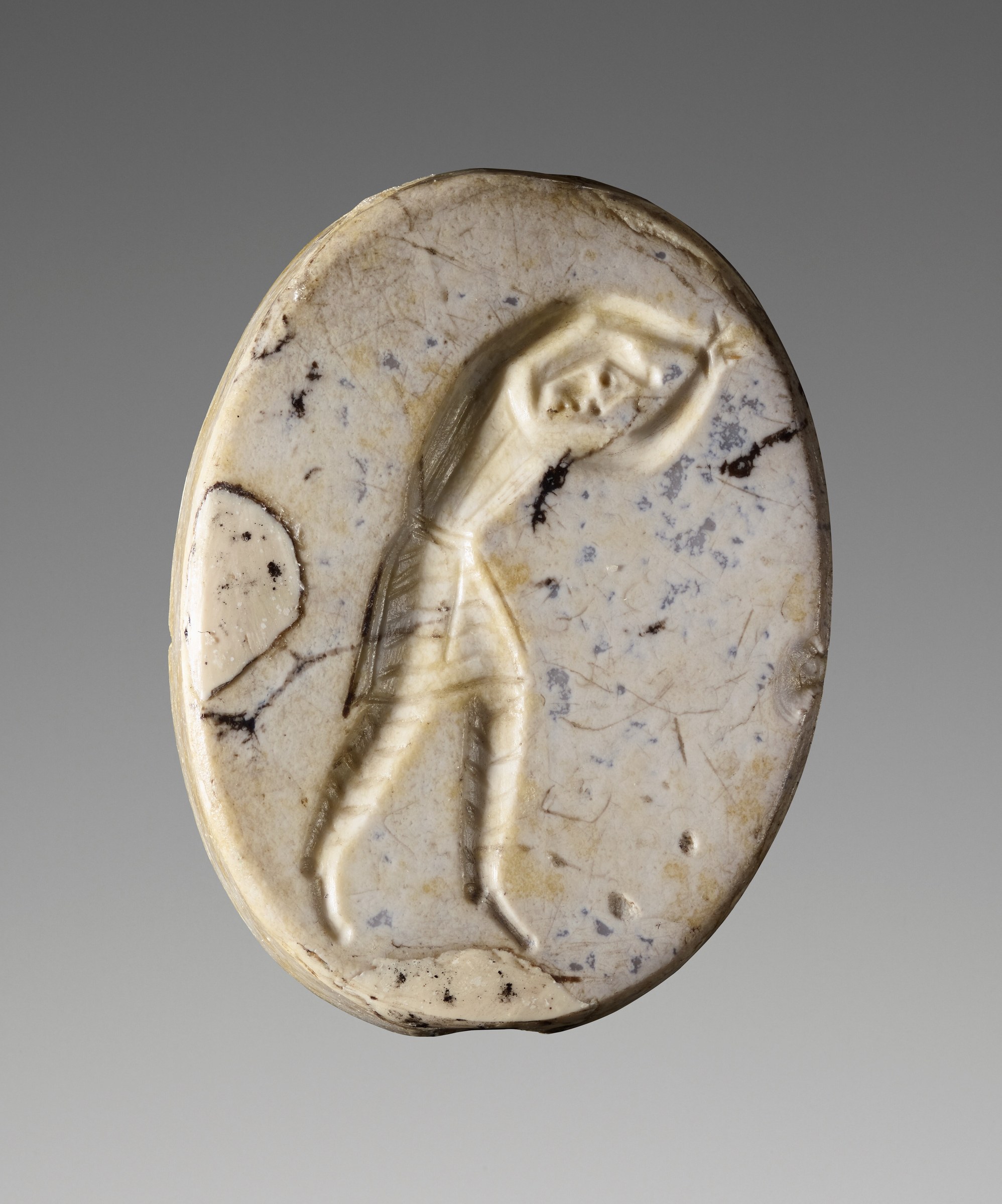Engraved chalcedony seal showing a Persian man in profile with raised arms, wearing a soft cap and tunic.