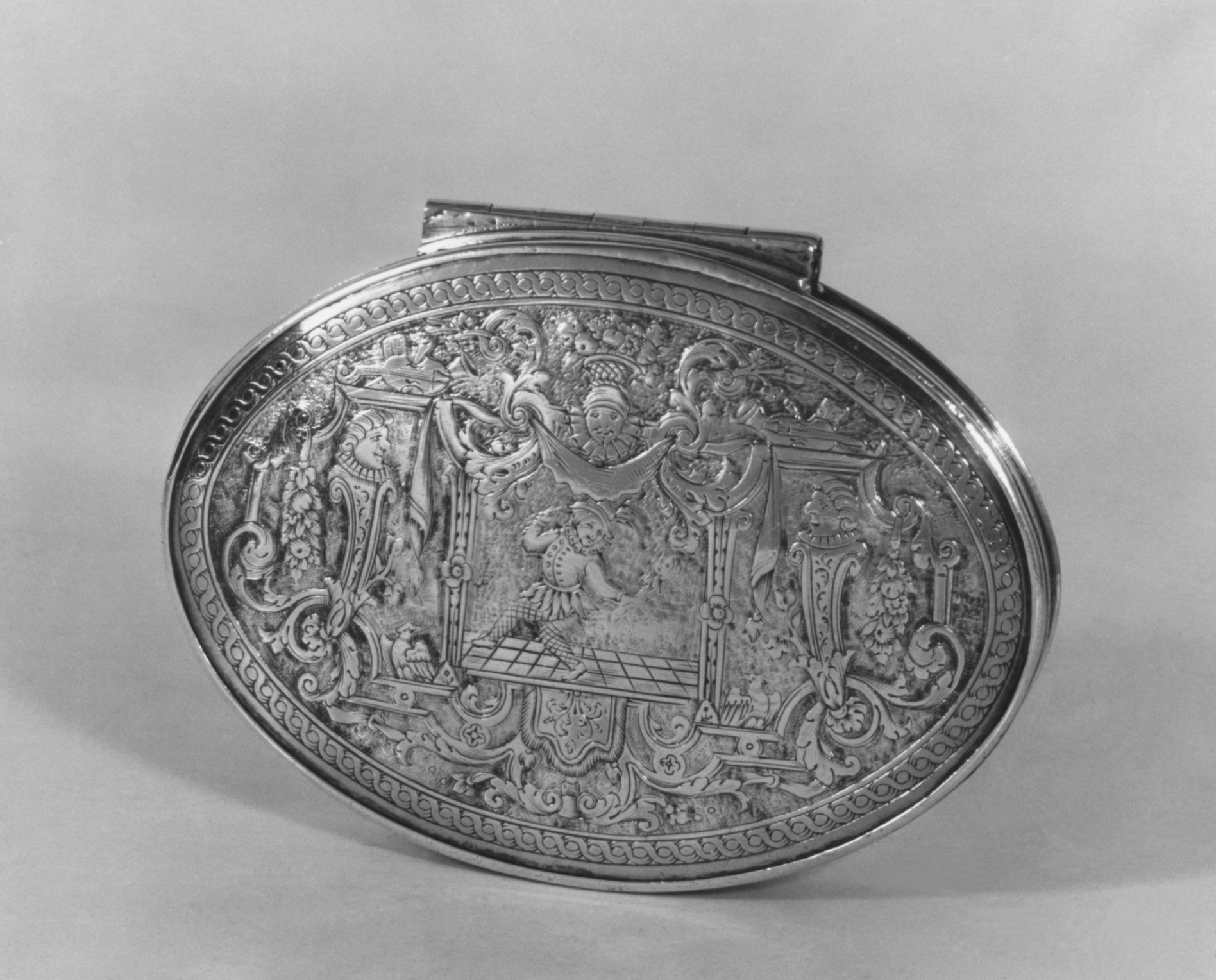 Ornate oval silver snuffbox with engraved scene of three figures in formal dress in a classical interior, surrounded by decorative scrollwork borders