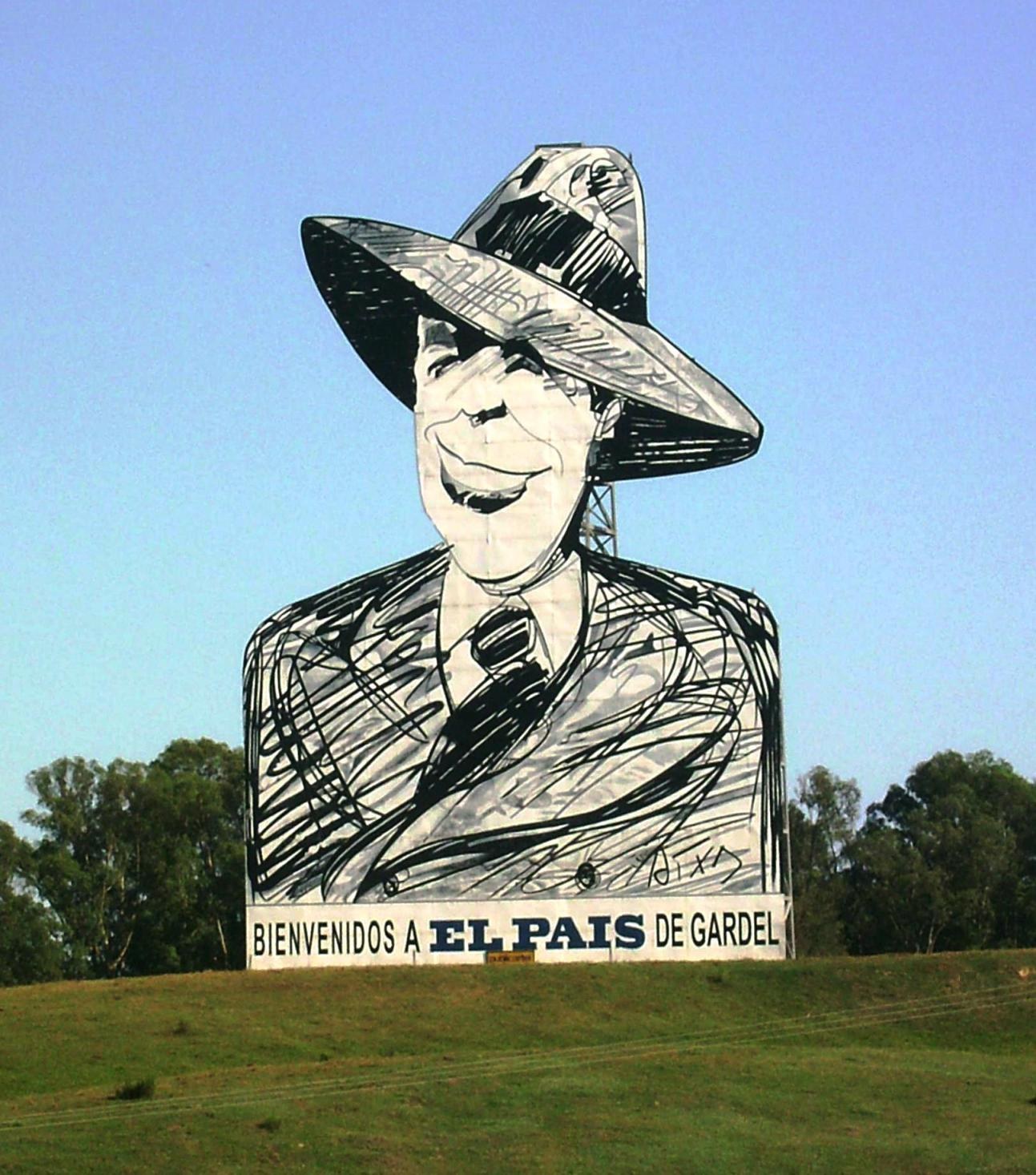 Caricatured portrait of a grinning man in oversized gaucho hat on a rural roadside monument, with text reading 'Welcome to the Land of Gardel'