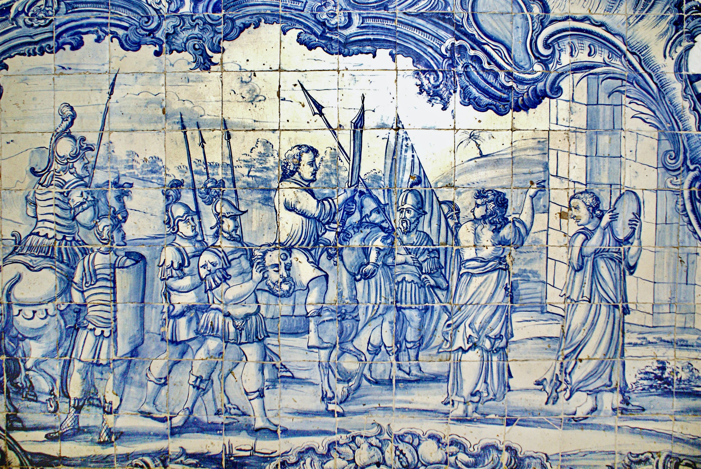 Cobalt-blue and cream Portuguese tile panel showing soldiers in military dress and standards surrounding a central figure in classical armor, within a