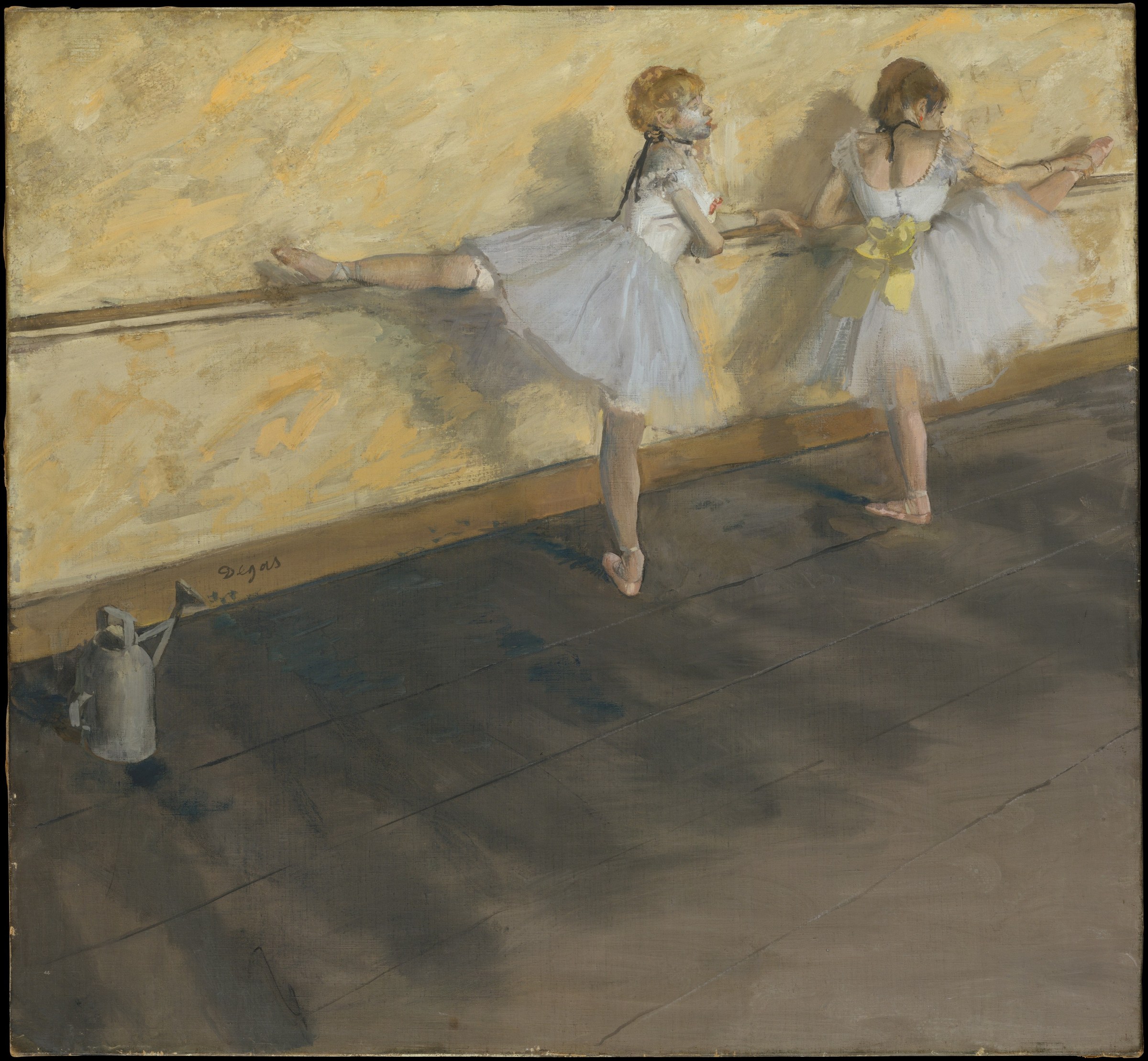 Two young ballet dancers in white tutus and pointe shoes stand at a wooden barre in a studio, legs extended and arms in classical positions.