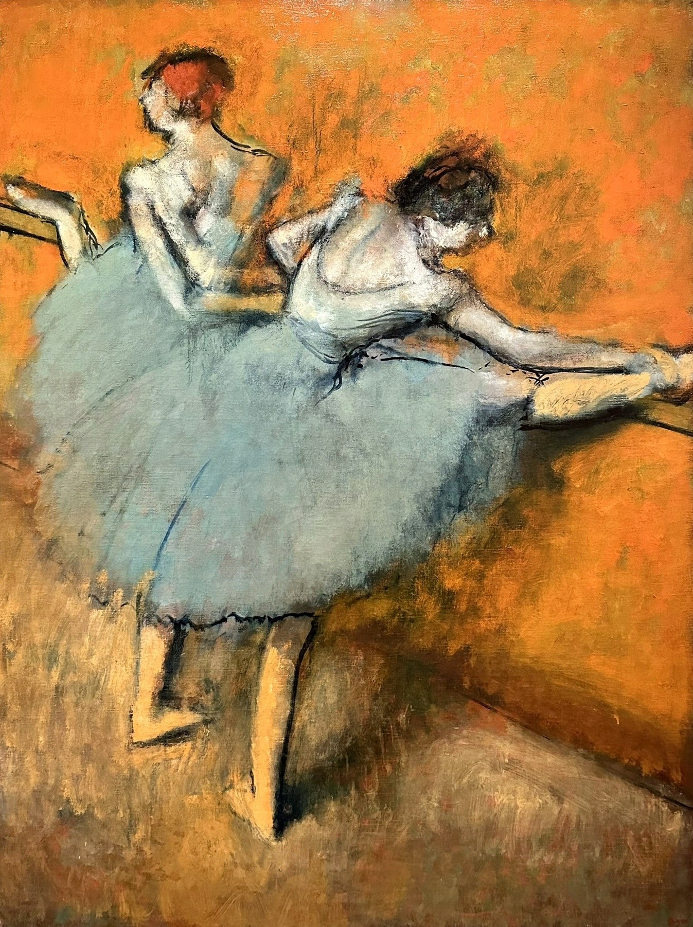 Two ballet dancers in pale tutus hold a wooden barre against a warm orange background, one extending her leg in a controlled position.