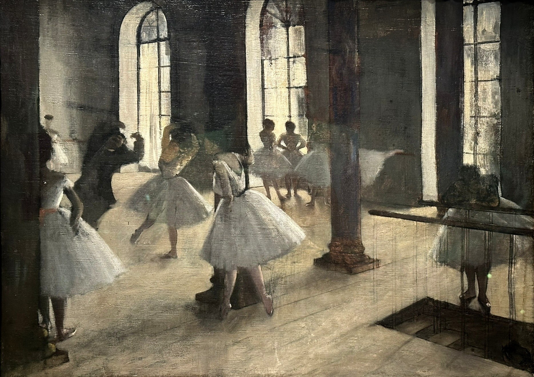 Ballet dancers in white practice dresses in a sunlit studio with tall windows, standing or moving at various distances in a pale, geometrically ordered space.