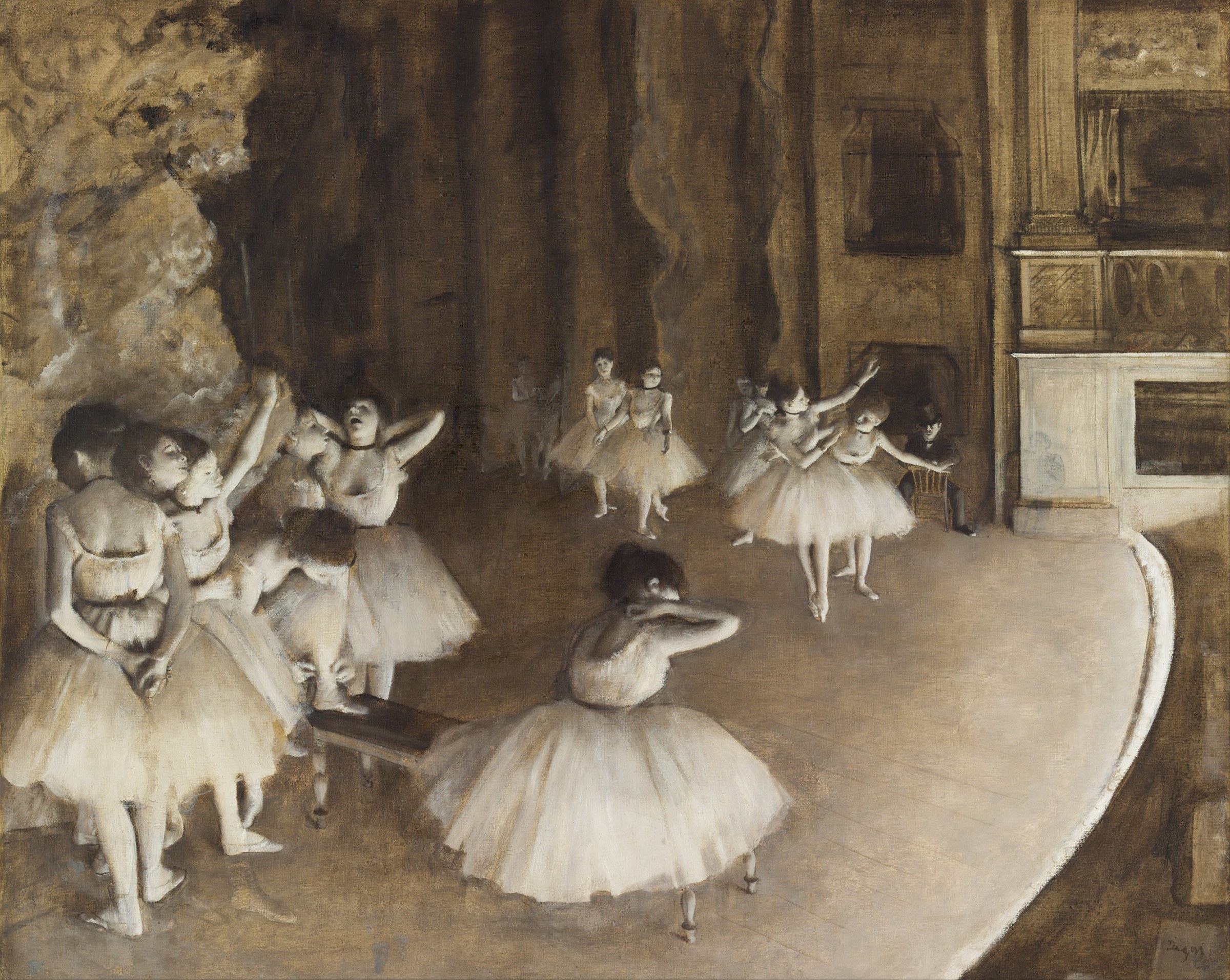 Multiple ballet dancers in pale tutus scattered across a stage lit by warm theatrical light, some en pointe or stretching.
