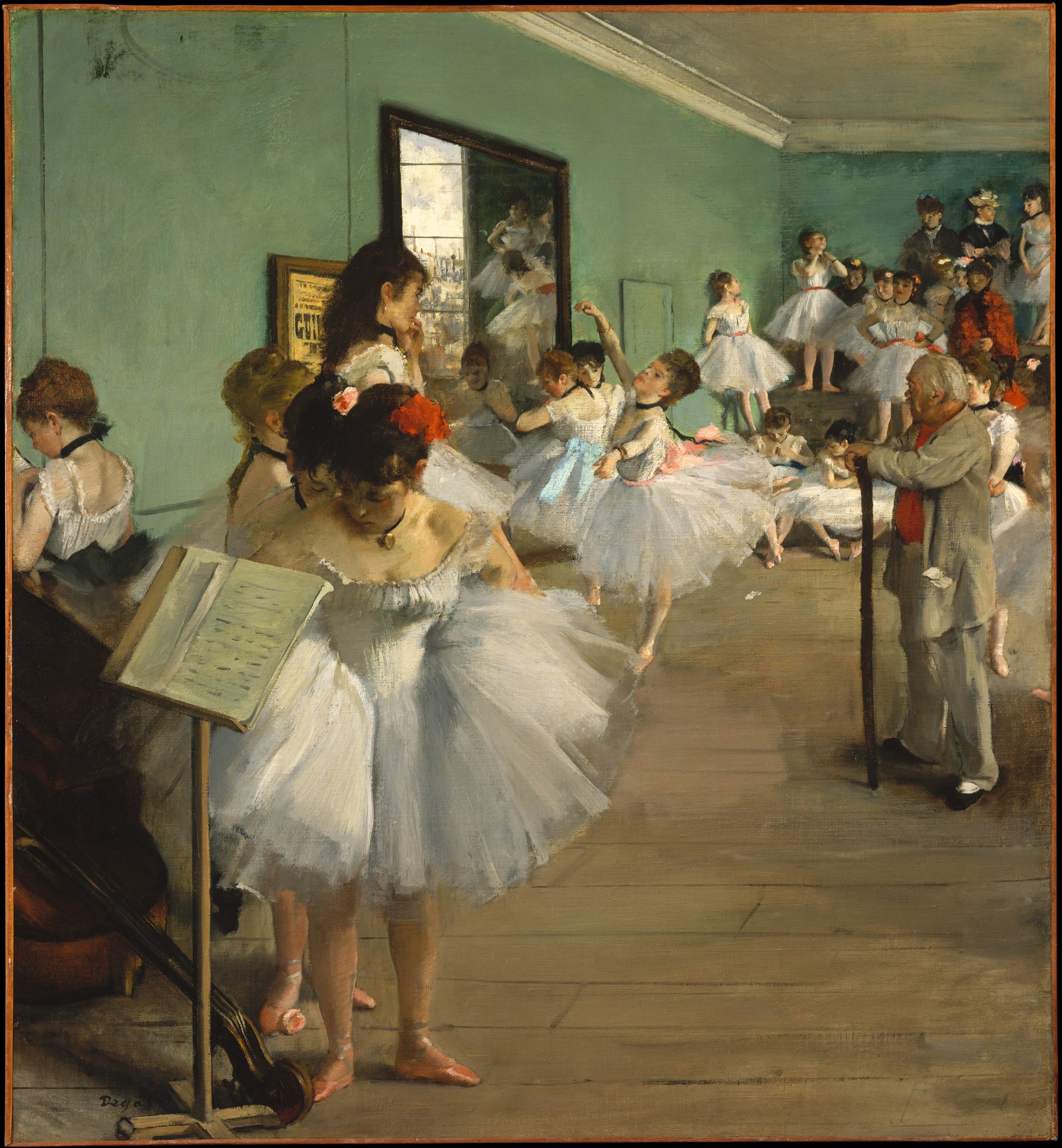A ballet instructor in a grey suit watches over a class of young dancers in white tutus and pointe shoes practising in a light-filled studio with pale green