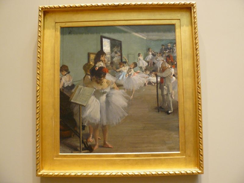 Ballet class in a studio: young women in white tutus and pointe shoes, watched by a dark-clothed male instructor standing apart.