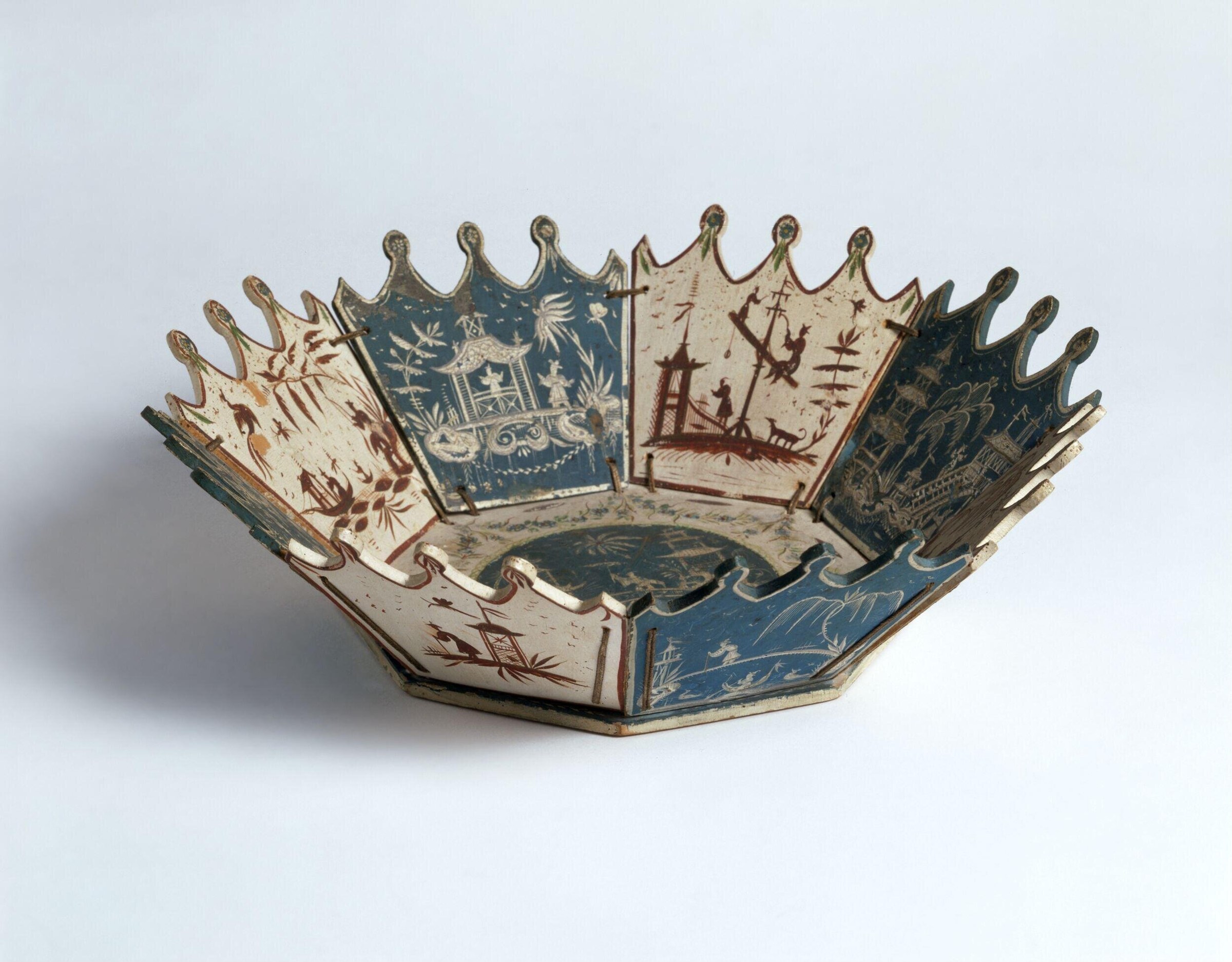 Scalloped lacquered box with eight flared panels painted with Chinoiserie landscapes and tiny figures, cream and blue ground with rust-red and gilt details.