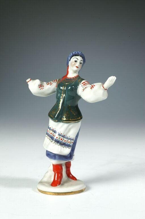 Porcelain figurine of a Ukrainian dancer in red boots and embroidered costume, arms raised, on a circular base.
