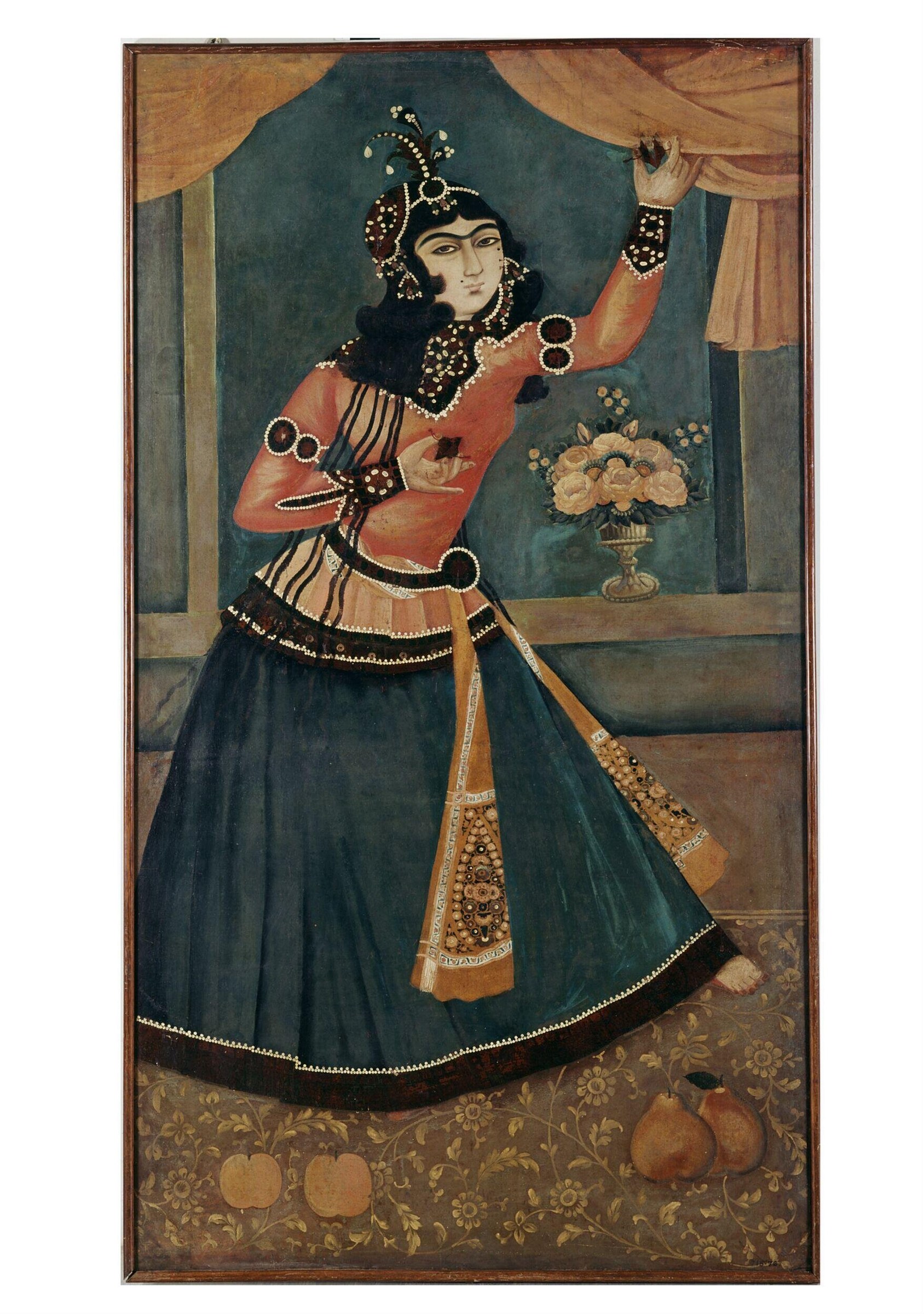 A woman in an ornate jeweled costume and headdress stands in a draped interior, one arm raised, facing forward.