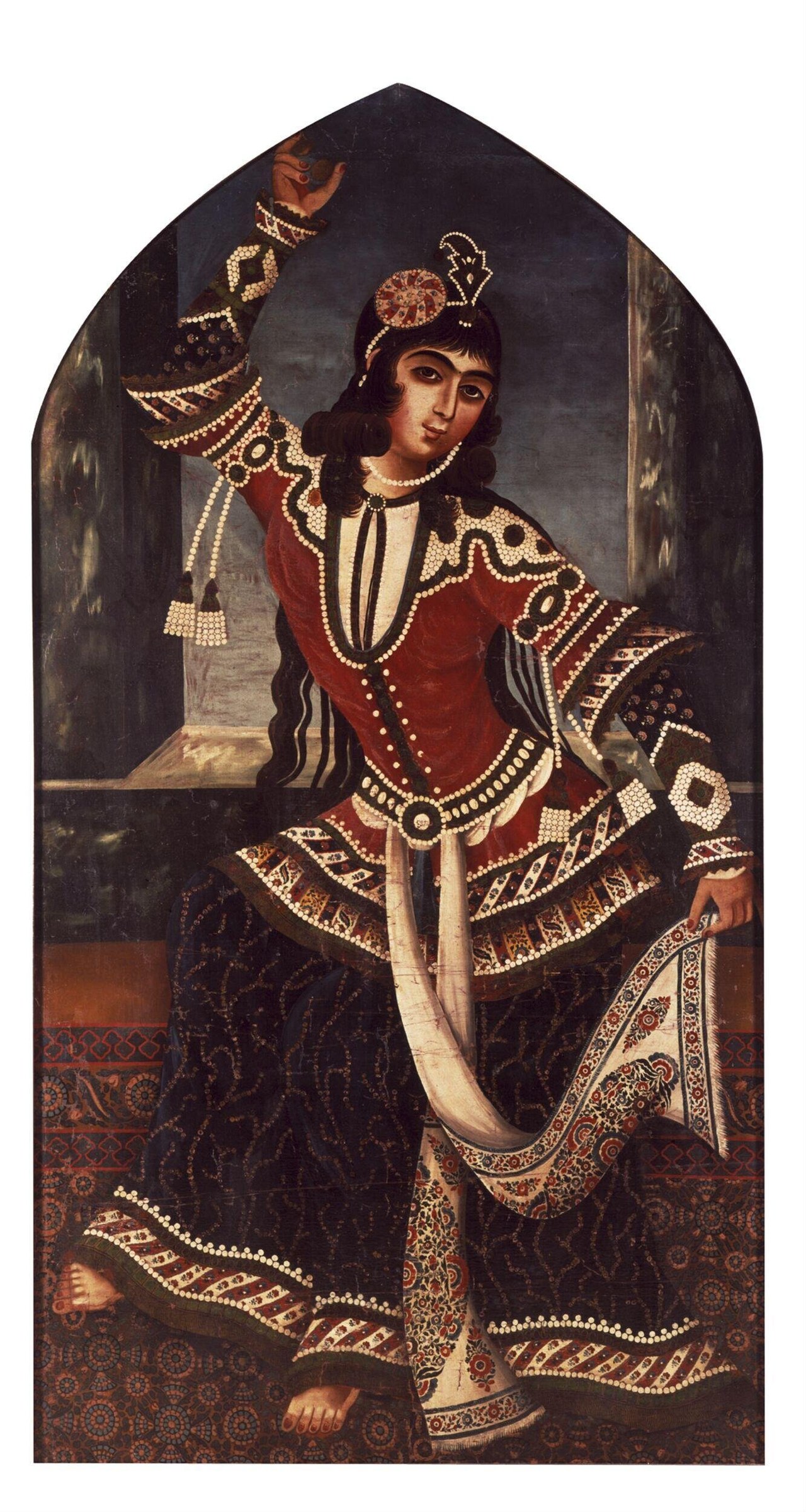 Woman in red silk embroidered dress and tall pearl headdress, posed mid-turn in arched stone room
