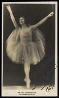 A performer in a pale tutu stands against a dark background, left leg extended to the side, both arms open, in a classical ballet pose.