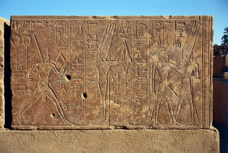 Limestone relief showing an Egyptian queen in formal dress leaning toward a standing god figure, with hieroglyphic inscriptions.
