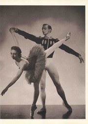 Black-and-white photograph: male ballet dancer in wide stance with arms extended, supporting a female dancer in arabesque in front of him.