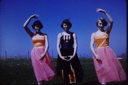 Three ballet dancers in classical poses against a twilight sky: one in dark costume with raised arms in center, two in matching pink tutus flanking her.