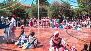 Outdoor folk dance workshop with dozens of people in casual dress dancing in close partner contact on red earth ground.