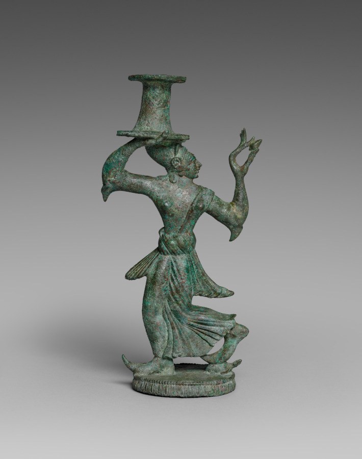Bronze candelabrum stand showing a twisted female figure in ecstatic pose with raised arm and vessel balanced on her head.
