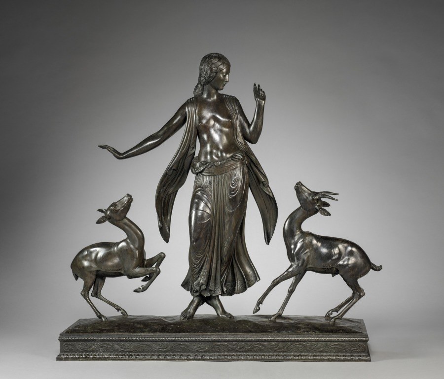 Bronze sculpture of a classical woman in contrapposto, arms extended, flanked by two leaping gazelles; mounted on a rectangular base.