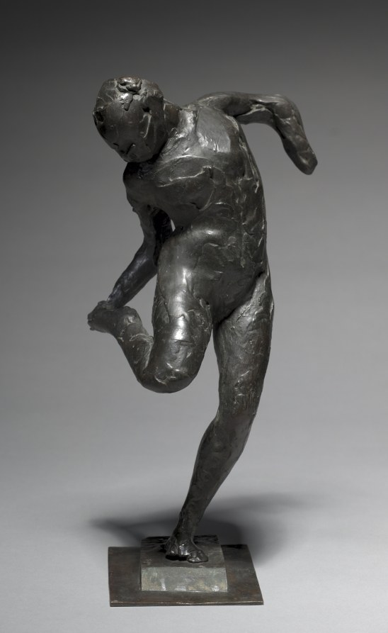 Nude female figure in dark bronze, standing in contrapposto with head bowed, gazing at her right foot