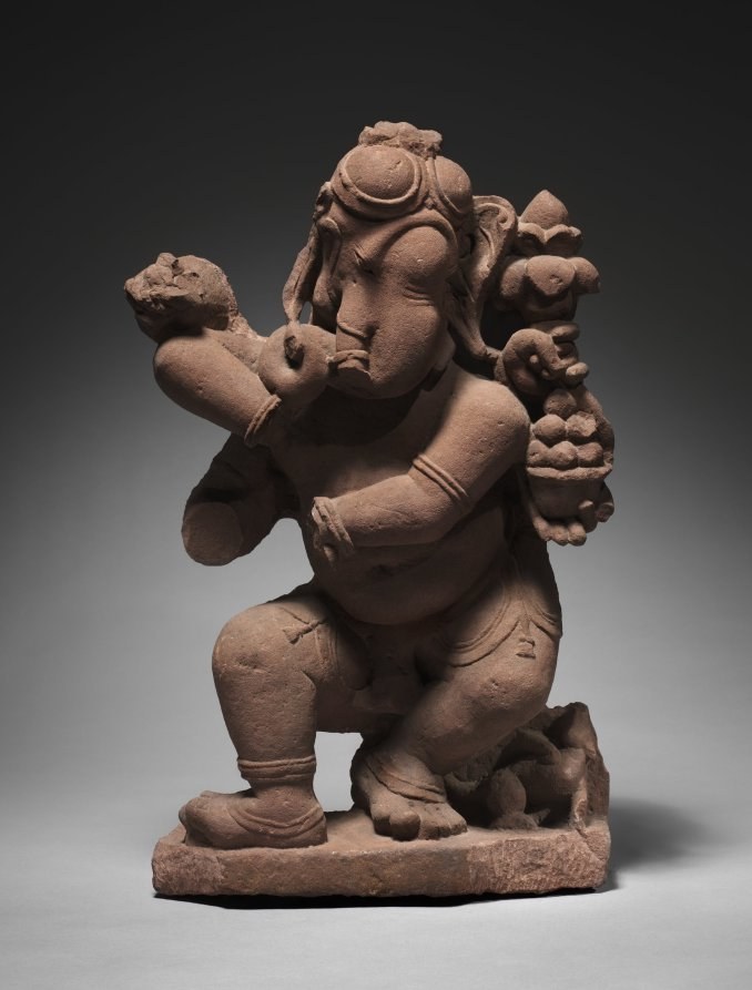 Terracotta sculpture of Ganesha with elephant head, bare torso, and four raised arms in a dynamic dancing pose on a rectangular base.