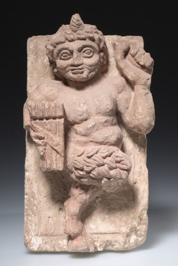 Stone relief carving of a muscular male figure with raised arm in a dynamic, wide-legged pose, head turned expressively