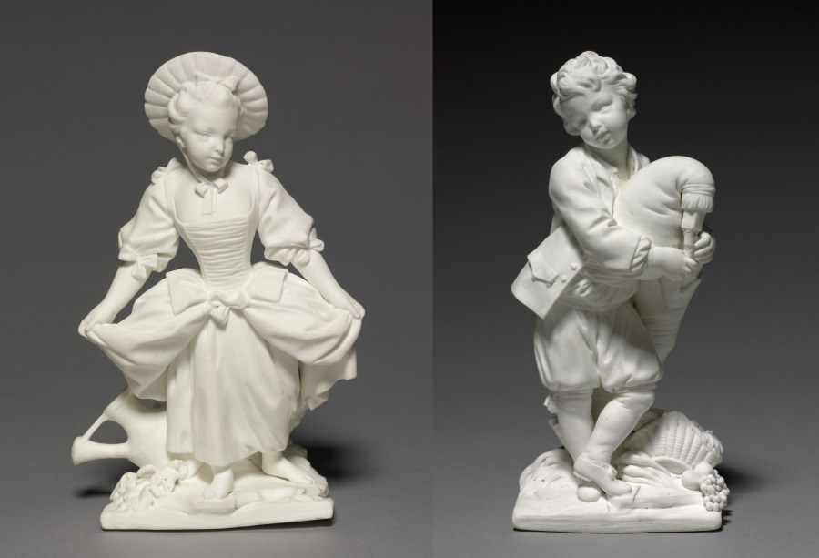 Two white porcelain figurines facing each other: a woman in an elaborate gown with winged headdress and a man in knee breeches holding a bagpipe.