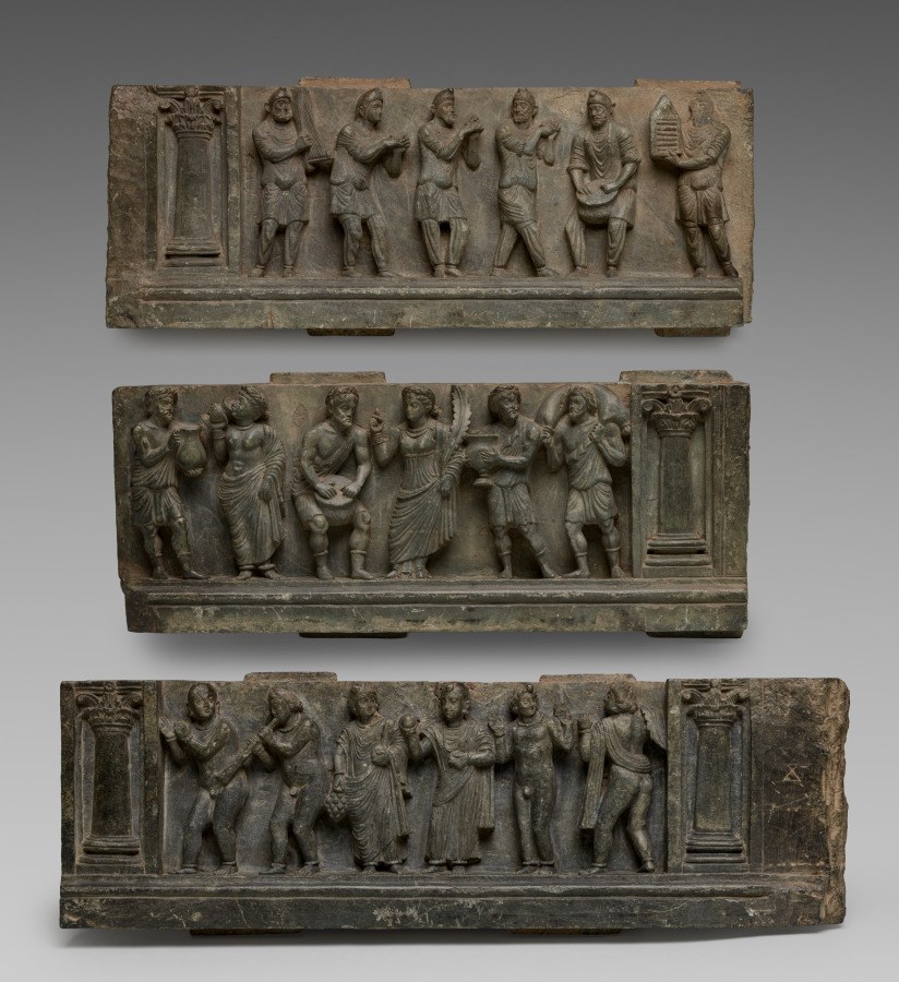 Three stacked stone relief panels showing figures in draped dress gesturing, dancing, and making music in scenes of celebration.