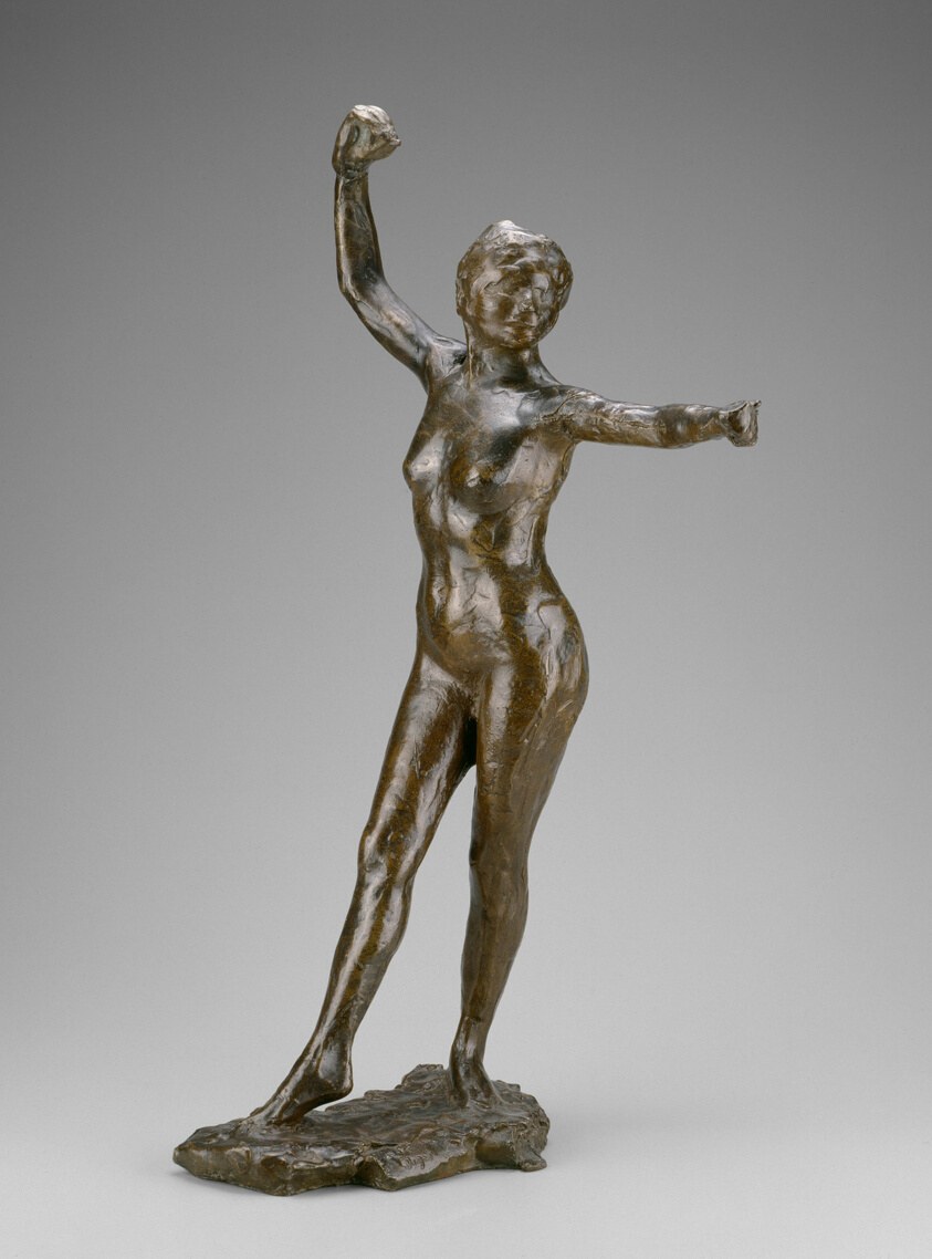 Bronze sculpture of a female nude with weight on her right leg, both arms raised in triumph, face upturned, standing on a textured base.