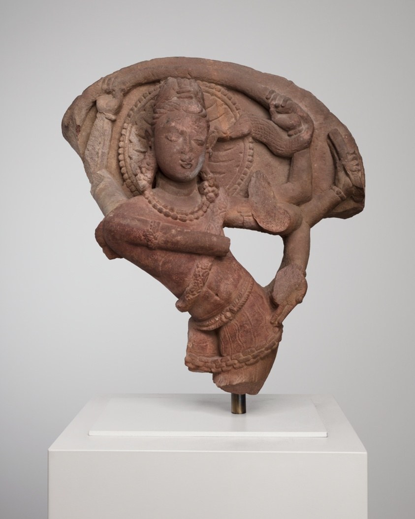 Terracotta fragment of an arched figure in profile wearing beaded ornaments, arms raised in a dance pose, framed by a curved arch above.