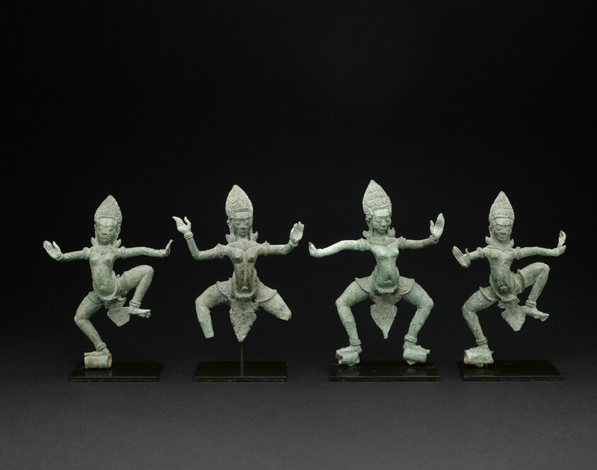Four bronze apsara figures in alternating leaping and deep squatting poses, arms extended, wearing elaborate crowns, mounted on black bases.