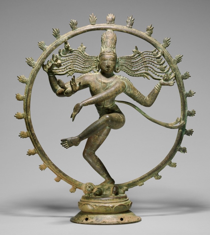 Bronze sculpture of a four-armed figure in dynamic spiral pose within a ring of radiating flame forms, standing on a lotus base.