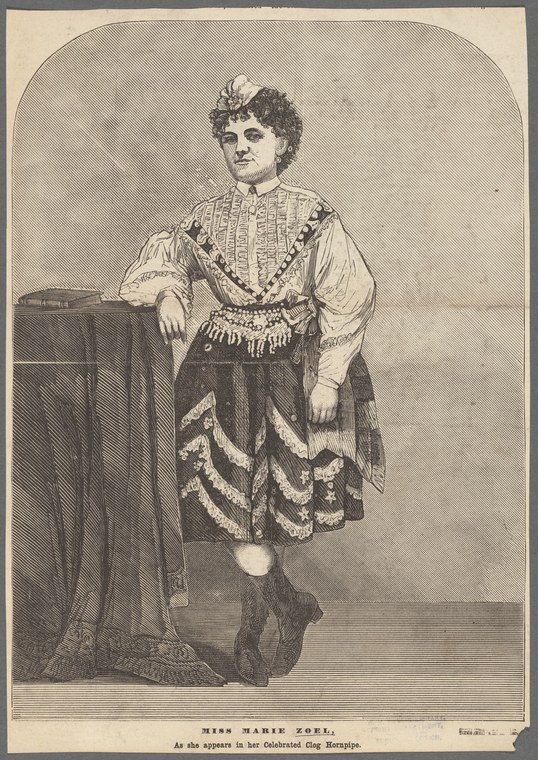 Woman in Victorian costume standing in performance pose, wearing a white chemise and dark decorated skirt, small white cap, posed as if about to dance.