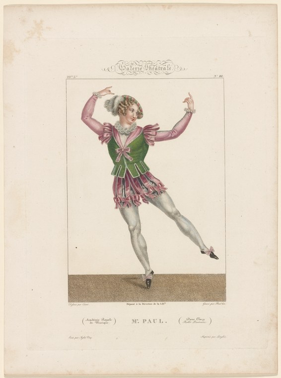 A blonde dancer in a green tunic and pink skirt leaps high with both arms raised, suspended against a neutral background.