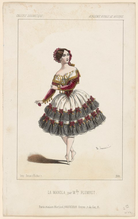 A woman in an elaborate 19th-century Spanish-style ballet costume stands in pointe position, one arm extended, against a plain background.