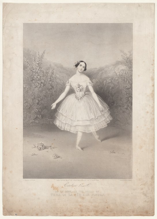 A woman in a white Romantic-era ballet costume with a short tulle skirt stands in a garden, balanced on one leg with her other leg extended.