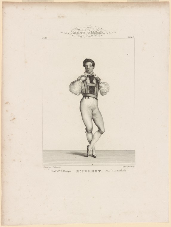 Male dancer in dark tunic and tights on pointe, arms raised in rounded position, facing forward on bare stage.
