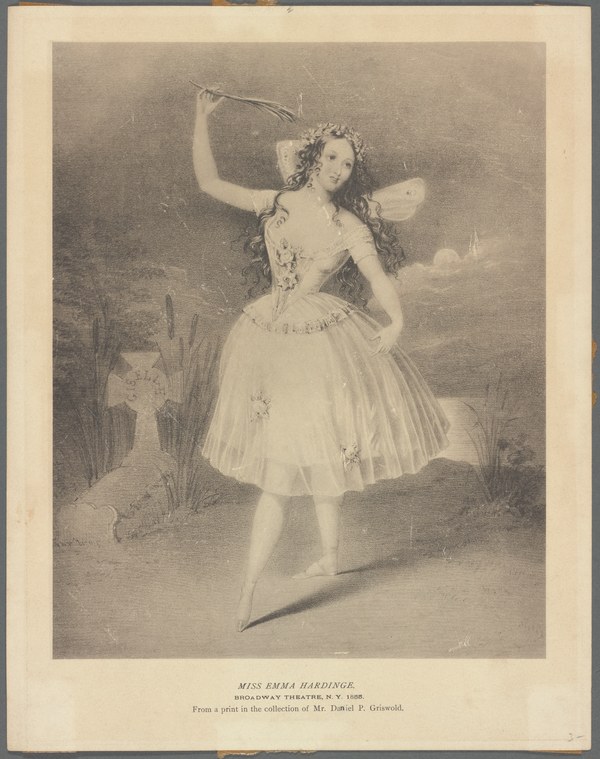 Woman in white tulle and fairy wings stands poised on one leg, arm raised, against a misty background, wearing a floral crown.