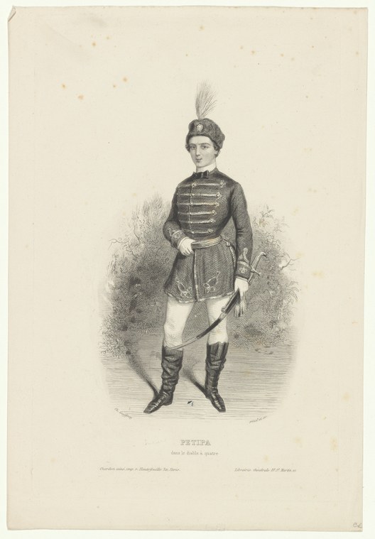 Male ballet dancer in dark military tunic with plumed hat and boots, standing in formal pose with raised arm, holding a curved sword.