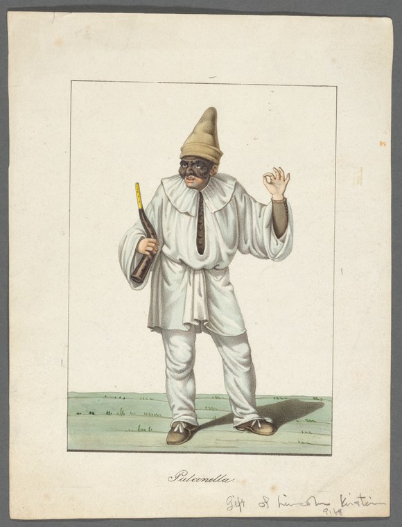 A man in white costume and tall yellow hat holds a small stick and raises his right arm in a theatrical gesture, wearing a mustache.