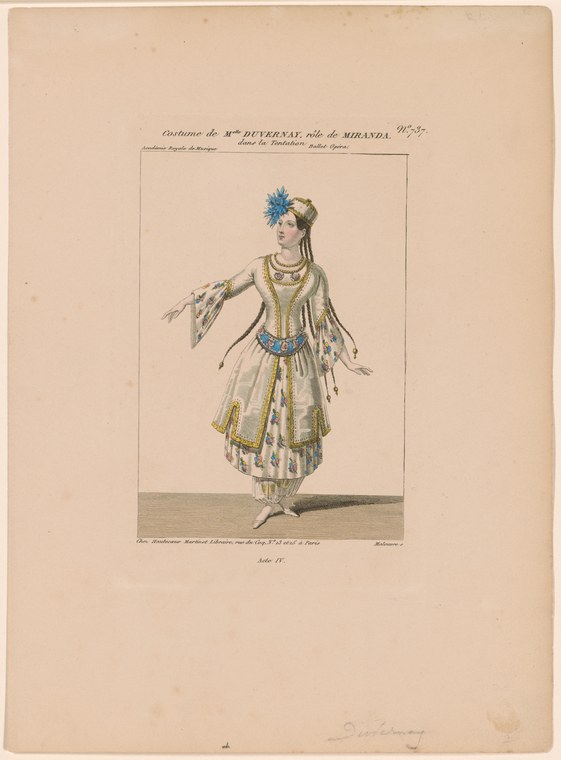 Woman in elaborate gold and blue theatrical costume with headdress and tasseled skirt, standing in frontal pose with left arm extended.