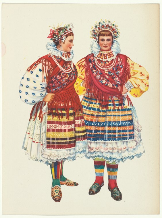 Two women in elaborately embroidered Yugoslav traditional dress with tiered skirts and ornate headdresses stand in formal poses.