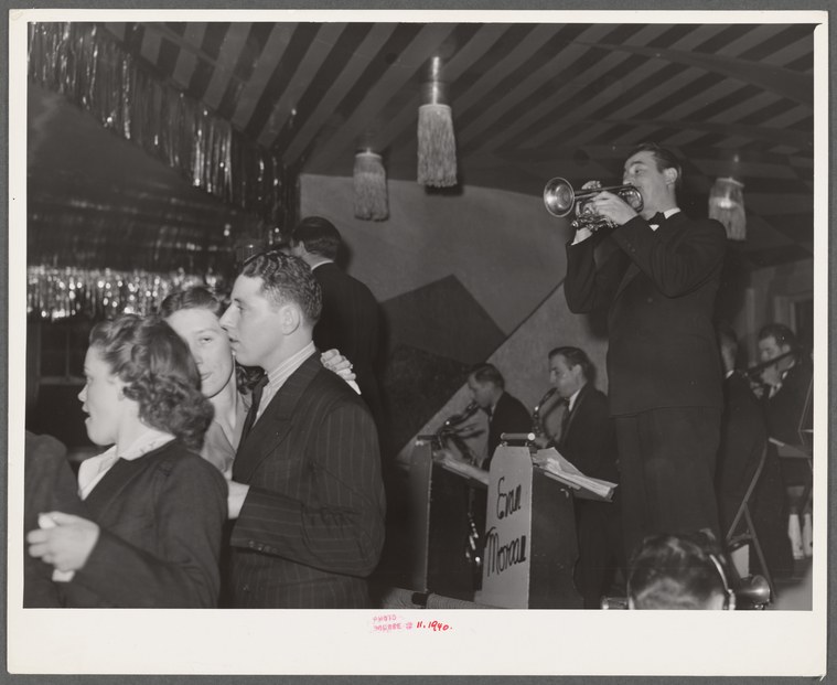 Black and white photograph of couples dancing closely together in a crowded 1940s dance hall while a live jazz band performs on stage.