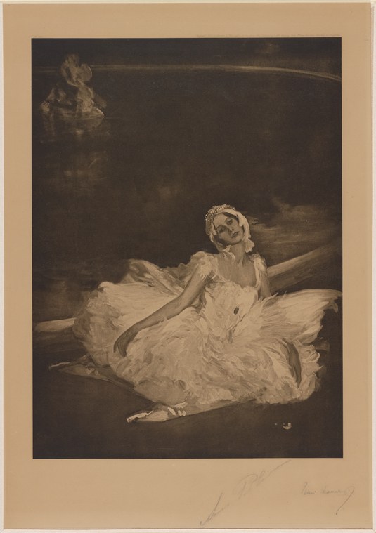 A female ballet dancer in a white tulle skirt reclines across a dark stage, her body extended and supported by one arm, her head tilted back in an attitude of