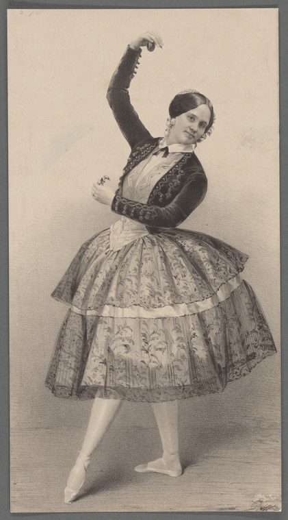 A woman in a dark bolero jacket and voluminous patterned skirt holds castanets, with raised arm in a graceful gesture, posed in a studio portrait.