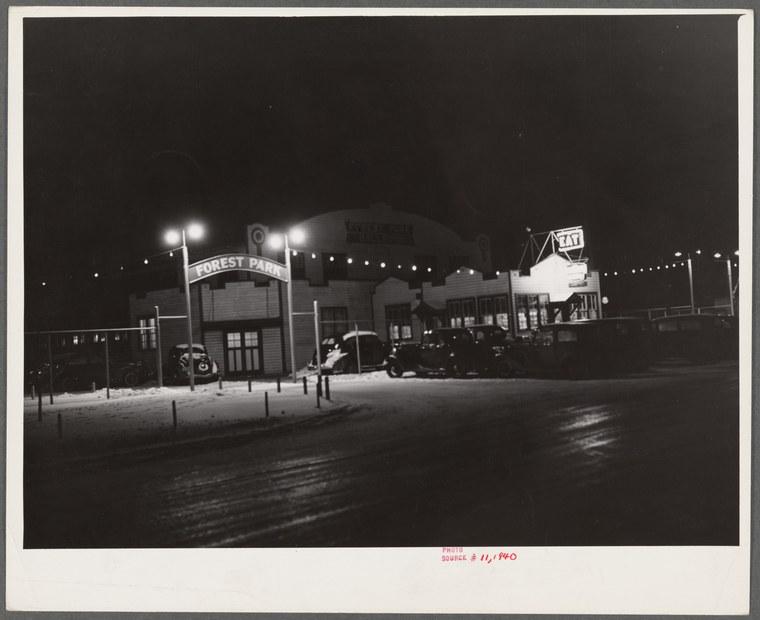 Night photograph of a small brightly-lit dance hall building in Marshalltown, Iowa, with parked cars and snow on the ground.