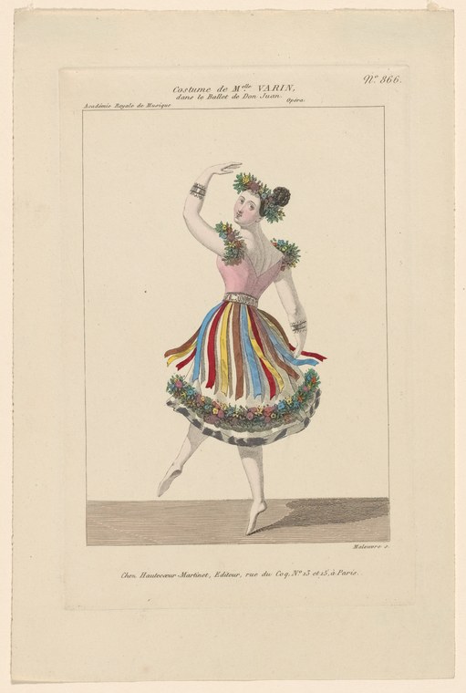 Young female dancer in pale pink bodice and multicolored ribbon skirt with green plume crown, posed en pointe with raised arms against neutral background.