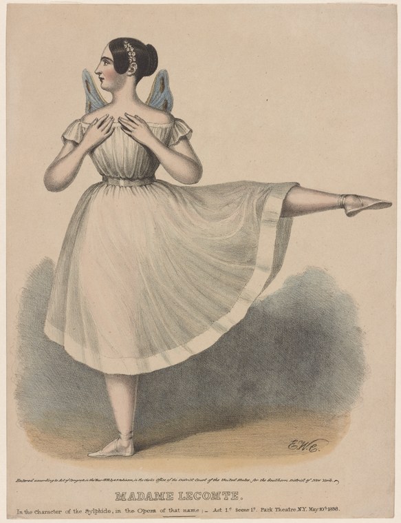 A female ballet dancer in a pale empire-waist dress with wings stands en relevé against a plain background, arms crossed at the wrists, head turned toward the